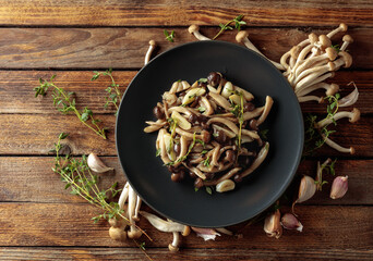 Fried shimeji mushrooms with thyme and garlic on a black plate.