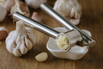 Garlic bulbs and garlic press on a wooden table.