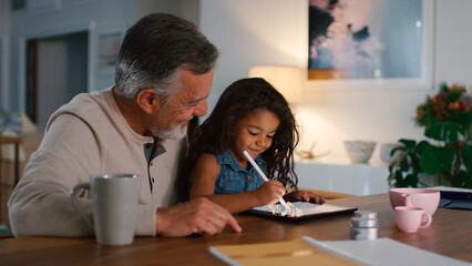 Grandfather With Granddaughter Drawing On Digital Tablet At Home