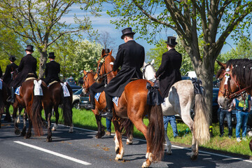 Sorbisches Osterreiten in der Lausitz. Festlich geschmückte Pferde und Reiter in schwarzer Festkleidung ziehen an einem Frühlingstag durch die Straßen.