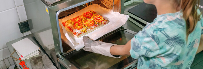 Banner of unrecognizable professional cook taking pizza out of oven in restaurant kitchen