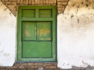Closed old Javanese wooden window with green shutters on an broken white concrete wall. Concept for traditional exterior, vintage, heritage, rural housing ornament. Empty blank copy text space.