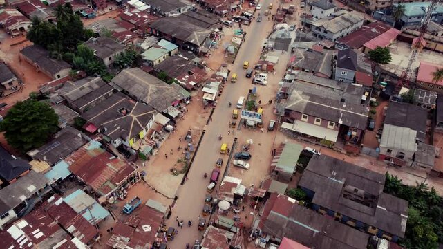 Agege, Nigeria - 26 July 2025: Aerial view of a bustling Akute - Ajuwon Road with cars and people amidst buildings with corrugated iron roofs, showcasing vibrant street life.