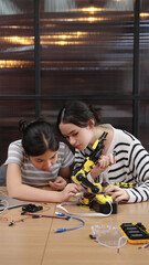 Asian and Caucasian girls collaborate on robotics project, assembling robot parts and sharing ideas...