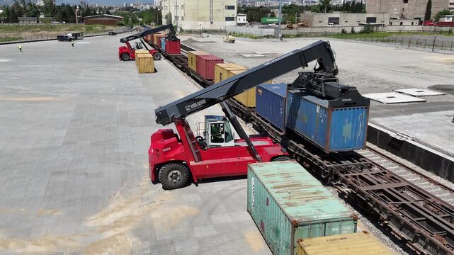 Aerial 4K drone footage of reach stackers handling shipping containers at a modern container terminal. Industrial port operations, cargo loading and unloading, logistics and transportation process in 