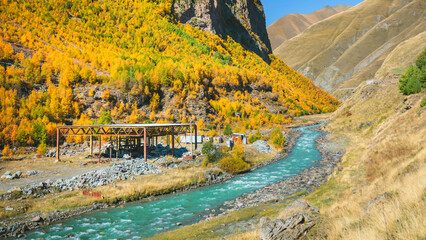 Colorful autumn valley with a fast-flowing river near Truso Gorge in Georgia. Golden foliage, dramatic cliffs, and rural life surrounded by majestic Caucasus mountains