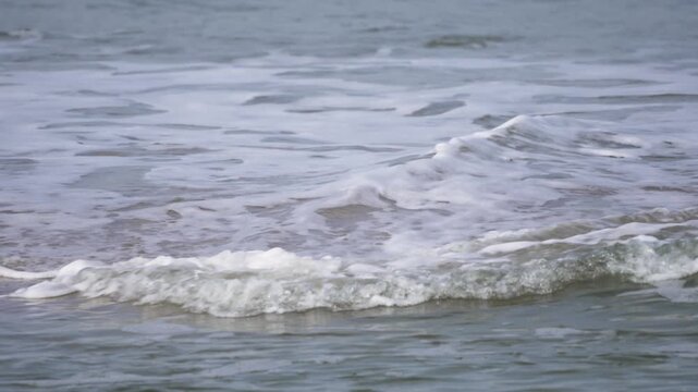 Rolling foam on the shore. Video shows foamy seawater washing gently onto the sandy beach, creating a calming and rhythmic coastal scene.