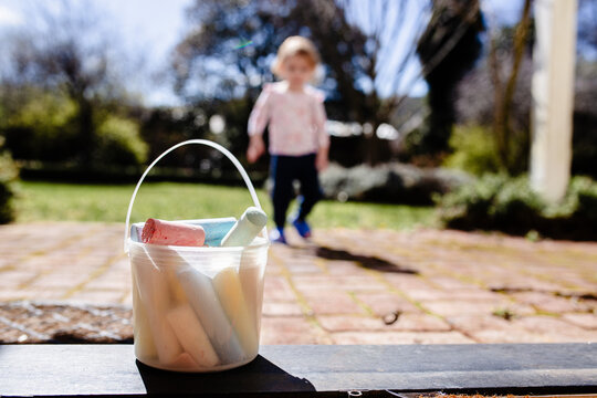 Plastic bucket filled with colourful chalk sitting on the patio