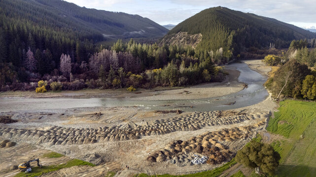Aerial view of a river winding through the Motupiko valley, flanked by dense forests and lined with mounds of gravel scraped from the recently flooded paddocks, Kohatu, Tasman region, New Zealand.