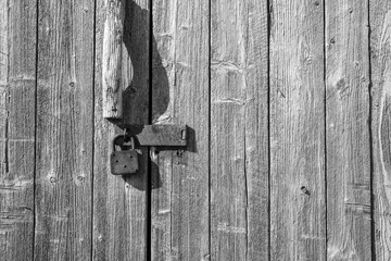 old wooden door with vintage hasp and paddlock in black and white vertical boards, weathered  suitable as background or banner  copy space room for text