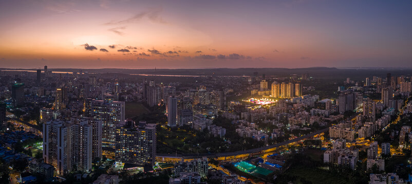 Aerial view of the cityscape with illuminated buildings casting a warm glow against the twilight sky, showcasing the urban sprawl, Mumbai, Maharashtra, India.