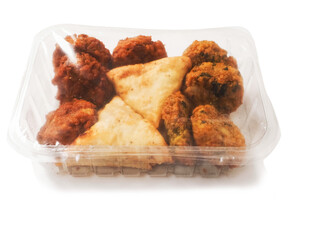 Indian style starter food selection of samosa, bhajis and pakoras in a plastic container on white background. Party sharing finger food made from fine products and aromatic spices. Orient vibe