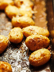 Cooked full uncut potatoes on a dark metal tray with herbs. Fine dinner side dish ready to be...