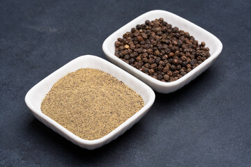 Black peppercorns  and ground black pepper powder on black background