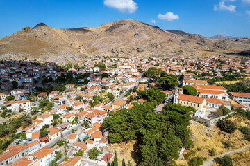 Aerial view of Eresos village on Lesvos island, Greece, with traditional red-roofed houses, dry hills, and clear blue sky, showcasing authentic Mediterranean beauty.