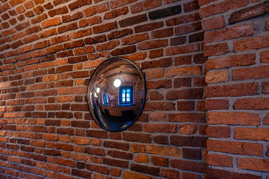Convex mirror in the hallway of a brick building.A brick hallway with a mirror on the wall.