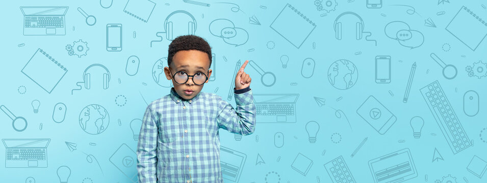 A young child stands confidently in a checkered shirt against a bright blue background filled with school-related items. He points up, showing enthusiasm for learning new things. - Powered by Adobe