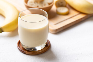 Banana milk in glass with sliced banana and fruit on white background