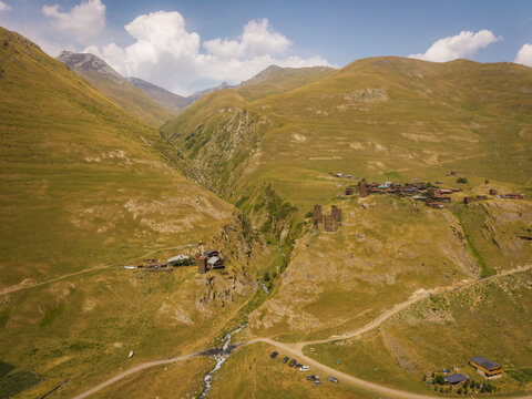 Aerial view of a rugged, sun-drenched valley with ancient stone towers nestled amidst rolling hills and a winding river, Parsma, Kakheti, Georgia.