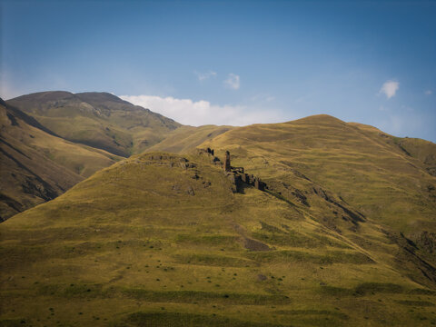 Aerial view of ancient stone structures nestled into the undulating green and brown hillsides under a bright blue sky, Dartlo, Kakheti, Georgia.
