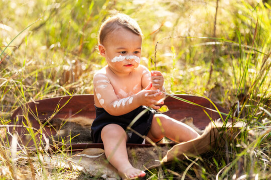 Happy little Aboriginal toddler boy sitting in coolamon in Australian bushland