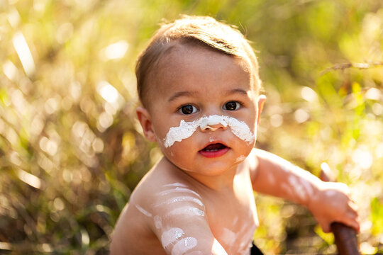 First Nations Australian boy among grass in natural bushland with clapsticks
