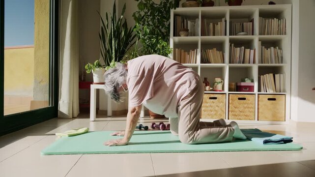 Elderly woman performing cat-cow yoga pose at home