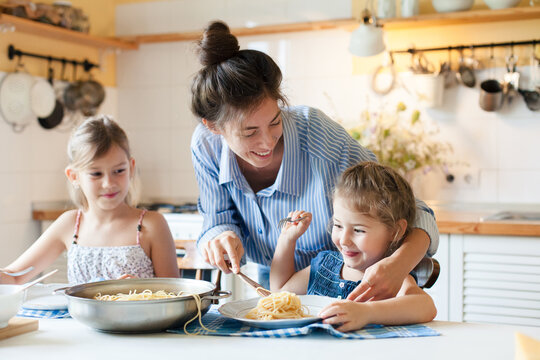 Happy mother serving pasta, feeding children at home kitchen. Cozy family lunch, solo motherhood, comfort food and healthy eating for kids. Homemade Italian cuisine. Authentic lifestyle moment
