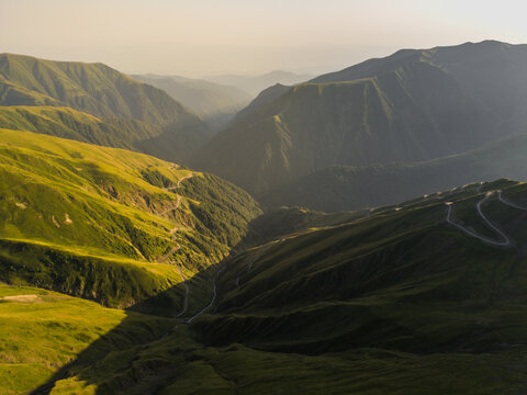 Aerial view of lush green mountains, with winding roads clinging to the slopes under a hazy sky, Alazani pass, Chala, Kakheti, Georgia.