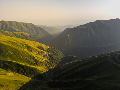 Aerial view of sun-kissed green slopes meet shadowy valleys in the Alazani Pass, a tapestry of light and shadow revealing the raw beauty, Chala, Kakheti, Georgia.