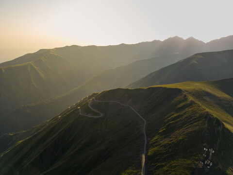 Aerial view of winding roads cutting through the verdant, sun-kissed mountains, a tapestry of light and shadow, Chala, Kakheti, Georgia.