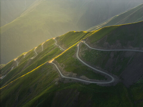 Aerial view of a winding road snaking across verdant hillsides, kissed by golden light at Alazani pass, Chala, Kakheti, Georgia.