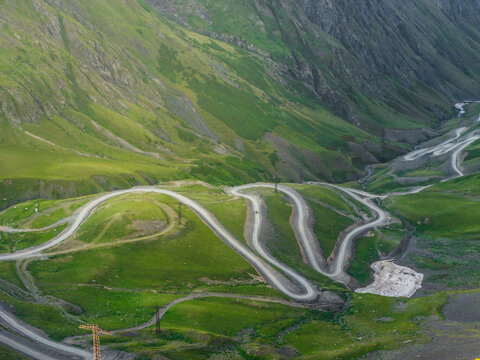 Aerial view of a winding road cutting through the rugged, verdant mountains, a stark white contrast against the deep green slopes, Chala, Kakheti, Georgia.