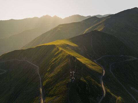 Aerial view of sun-kissed ridges and winding roads carve through the verdant peaks of Alazani Pass, Chala, Kakheti, Georgia.