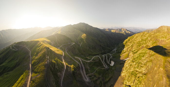 Aerial panoramic view of winding roads carving through the rugged, sun-kissed Alazani Pass, where green slopes meet the stark contrast of rocky peaks, Chala, Kakheti, Georgia.