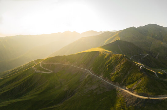 Aerial panoramic view of winding road snaking through the vibrant green hills under a golden sunlit sky, Alazani pass, Chala, Kakheti, Georgia.