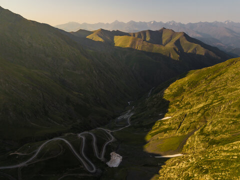 Aerial view of a winding road snaking through the verdant, sun-drenched Alazani Pass, where emerald valleys meet the towering peaks, Chala, Kakheti, Georgia.
