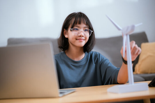 Young girl engages with a small wind turbine model at home, showcasing her interest in renewable energy and technology - Powered by Adobe