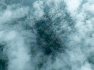 Clouds drift over a green landscape in Enshi City, Hubei Province, revealing hints of earth below.