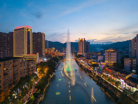Xuan'en County Hubei Province China city lights illuminate waterfront buildings and fountains in evening glow.