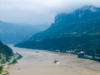 Yichang Three Gorges China river flows past steep mountains, carrying boats on its surface through a misty landscape.