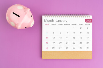 January 2026 desk calendar and pink piggy bank on purple background.