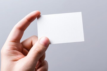 Obraz premium Vertical business card mockup in hand against a soft gray background, closeup shot highlighting texture and simplicity.