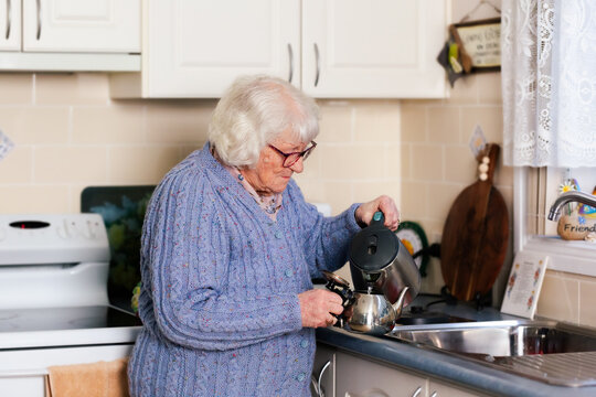 Older Aussie woman filling teapot in kitchen at home by the sink