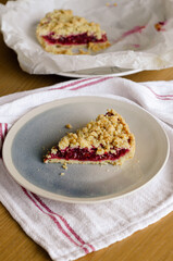 Close up of Italian sbriciolata crumble pie slice with organic plum jam on plate over white towel
