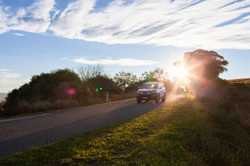 Car traveling down rural road with starburst of sunset light in rural Australia 