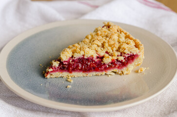 Close up of Italian sbriciolata crumble pie slice with organic plum jam on plate over white towel