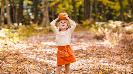 happy child girl throws autumn leaves and laughs outdoors with pumpkin on head