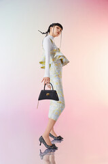 Stylish woman in modern outfit holding handbag, standing confidently against a soft pastel background.