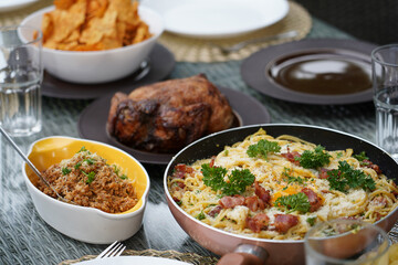 A delicious homemade feast on a dining table, featuring spaghetti carbonara, roasted chicken, and various side dishes. A concept for family gatherings and celebrations.